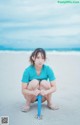 A woman crouching down on the beach with a blue umbrella.