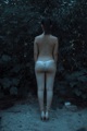 A woman in a white thong standing in the woods.