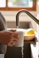 A person holding a cup of water under a faucet.