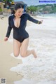 A woman in a black swimsuit jumping in the air on a beach.